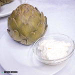cooked artichoke on plate with small bowl of mayo for dipping.