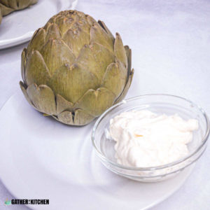 cooked artichoke on plate with small bowl of mayo for dipping.