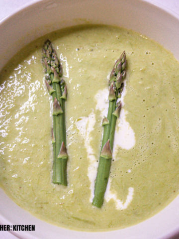 top down view of a bowl of creamy asparagus soup with a drizzle of cream in it as well as two tips of asparagus stalks.