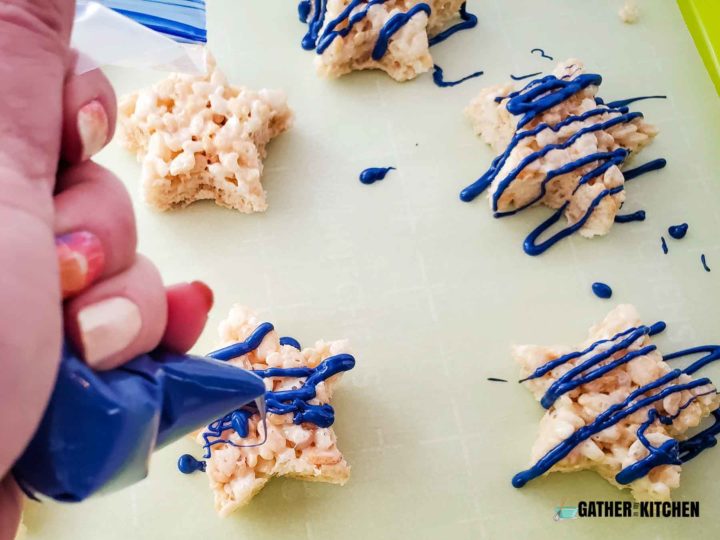Piping melted blue candy melts onto Rice Krispy stars.