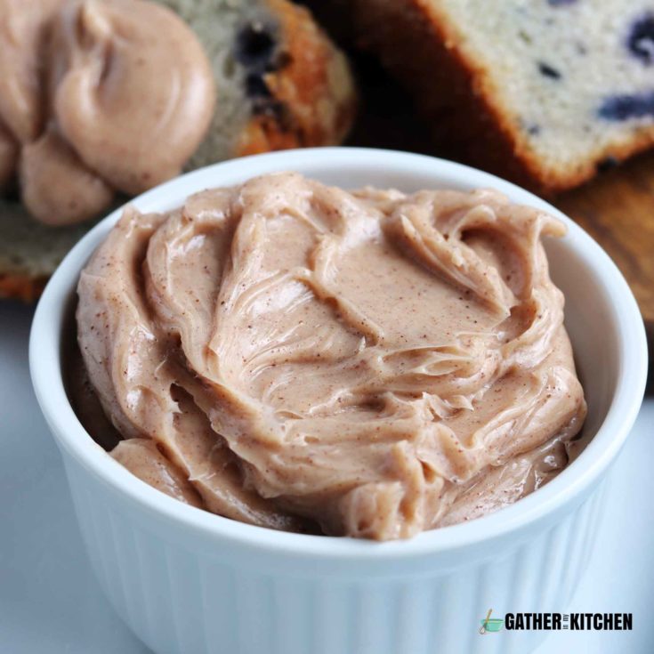 small container of honey cinnamon butter with slices of blueberry bread in the background.