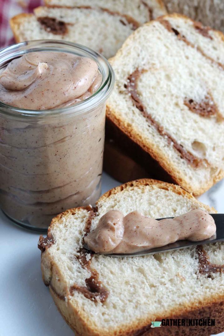 slice of cinnamon bread with a knife of honey cinnamon butter on it.  Jar of honey cinnamon butter with more bread in the background.