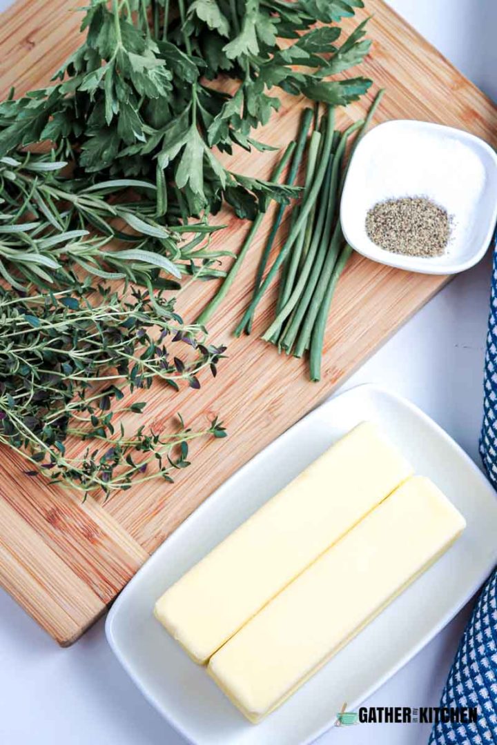 Cutting board with herbs, small bowl of salt & pepper, knife, spatula, mixing bowl with 2 sticks of butter.