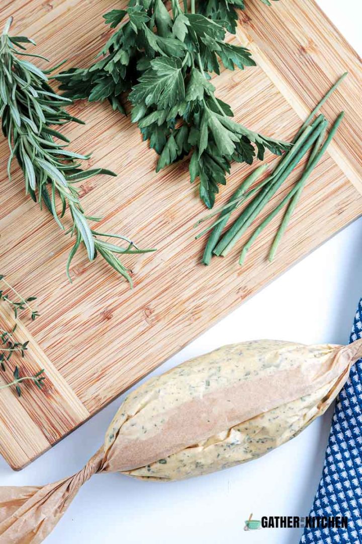 Cutting board with herbs, butter rolled up in parchment paper.