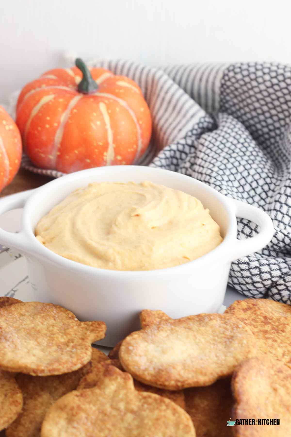 Bowl of pumpkin dip with pie crust chips in front.