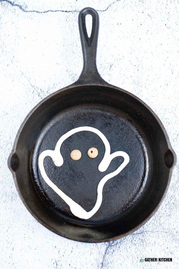 Skillet with pancake batter eyes and outline of a ghost.