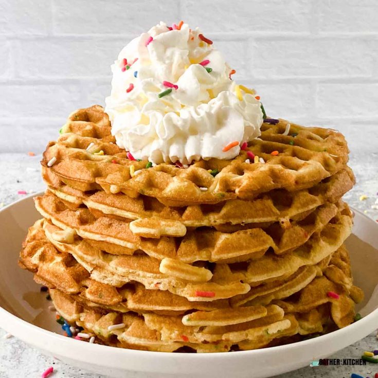 Stack of waffles with whipped cream and sprinkles on top.