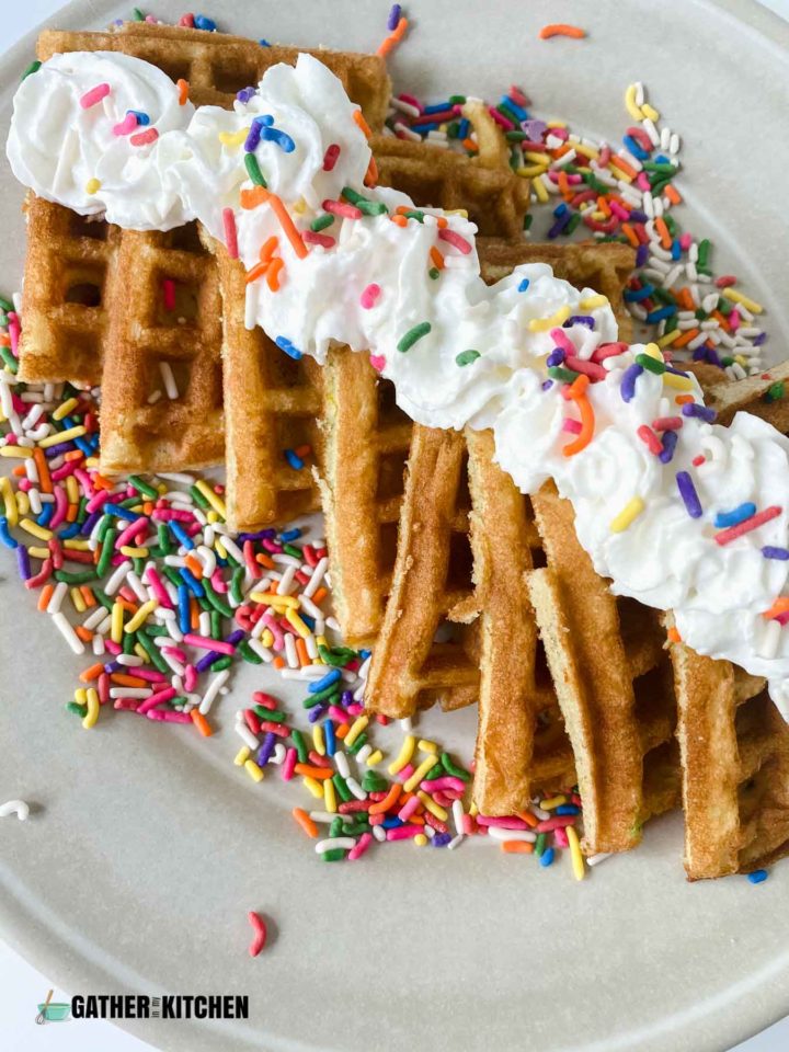 Waffles cut into triangles on plate with whipped cream and sprinkles.