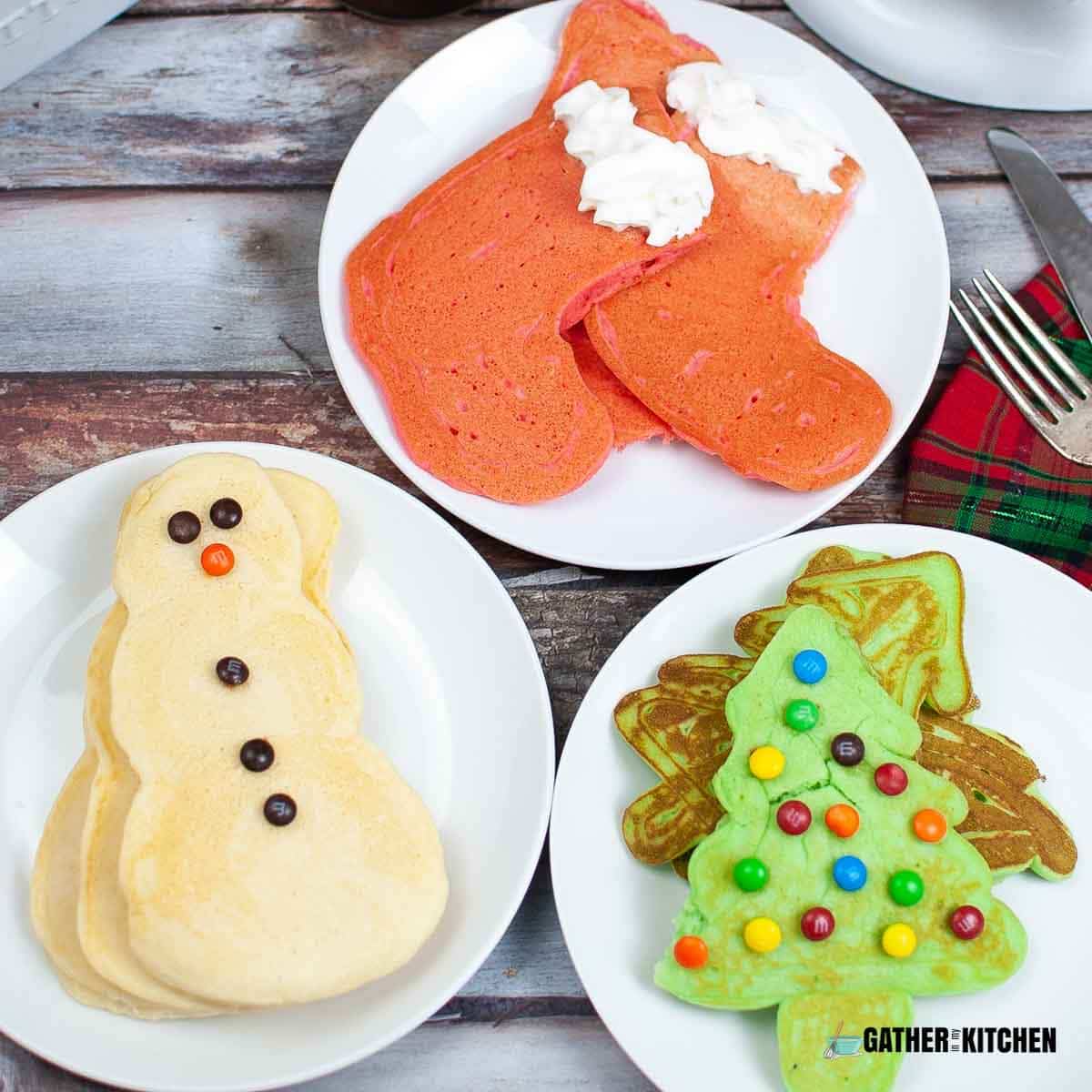 Christmas shaped pancakes on three plates - one stocking, one with snowmen pancakes, and one with Christmas tree pancakes.