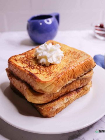 French toast stacked on plate with a dollop of whipped cream.