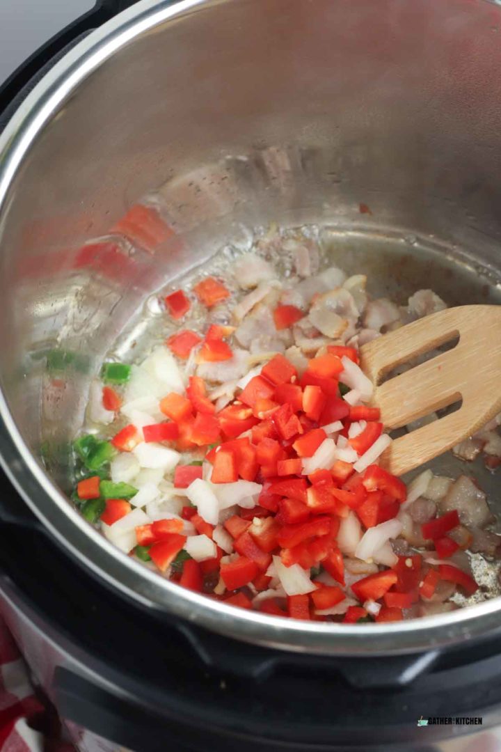 Stirring onions, jalapenos, bell peppers, and bacon in Instant Pot.
