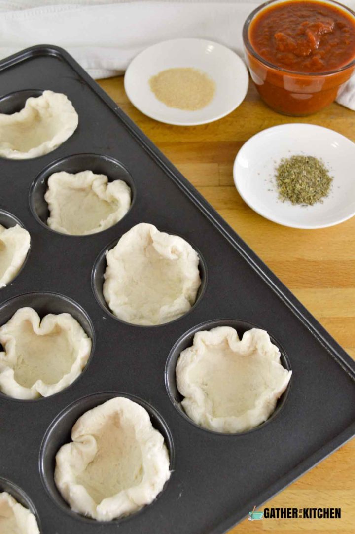 Muffin tin with biscuit dough in each cup.