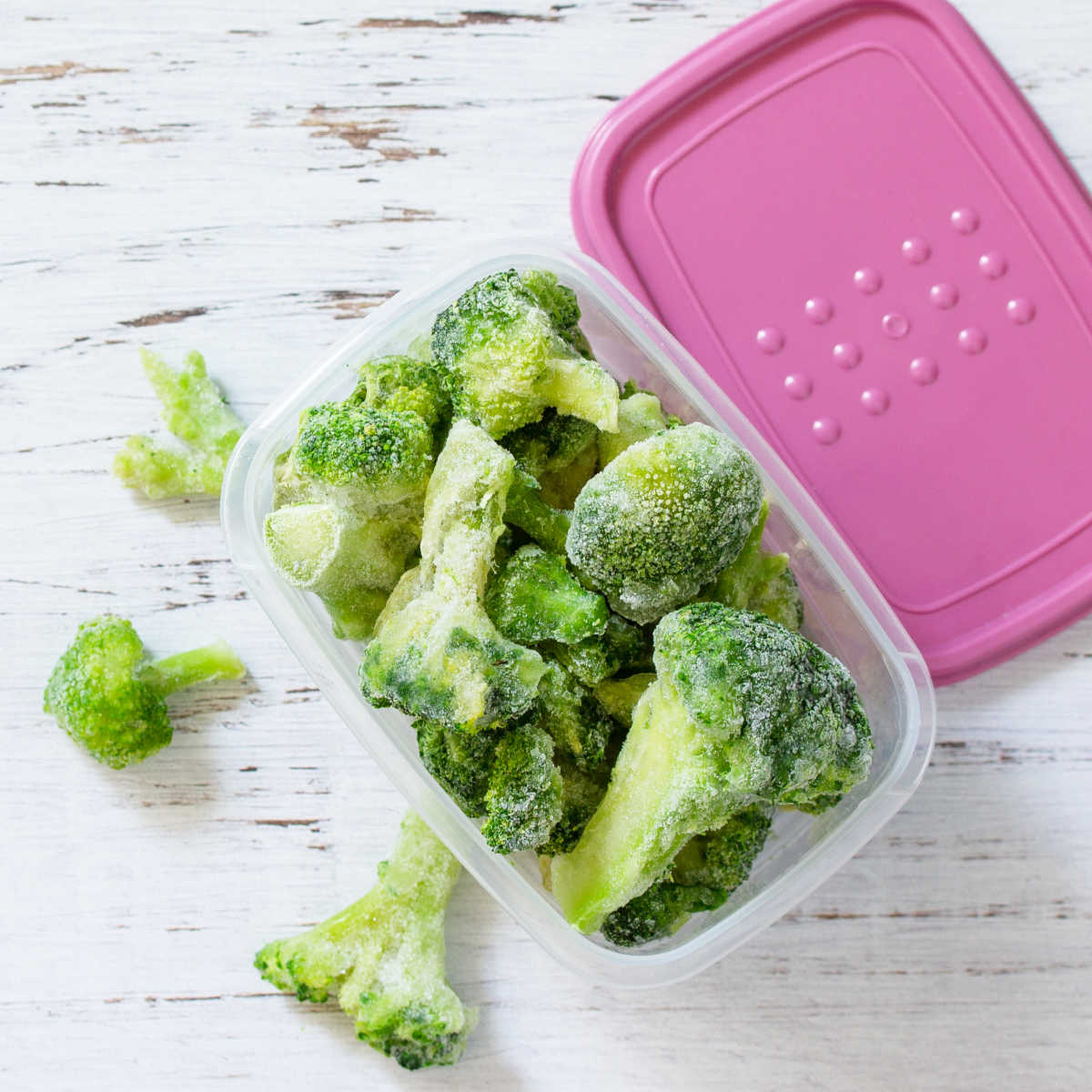 Plastic container overflowing with frozen broccoli.