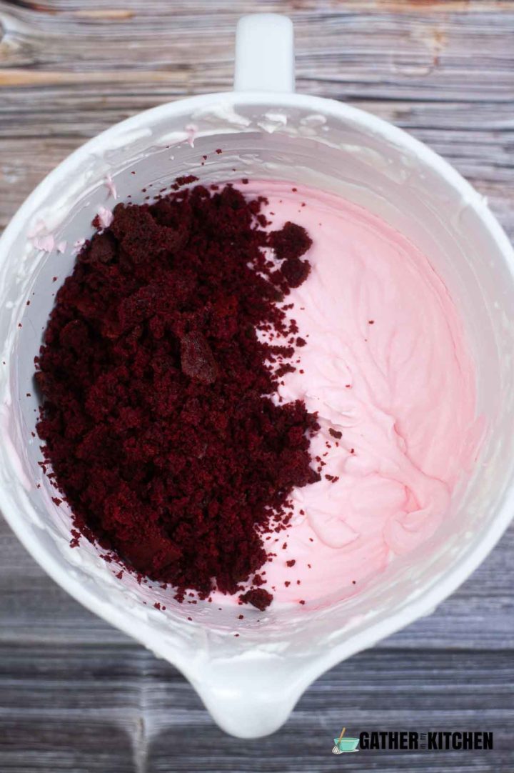 Red velvet cake crumbles being added to ice cream ingredients bowl.
