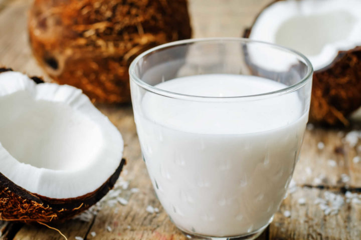 Coconut milk in cup with open coconuts next to.