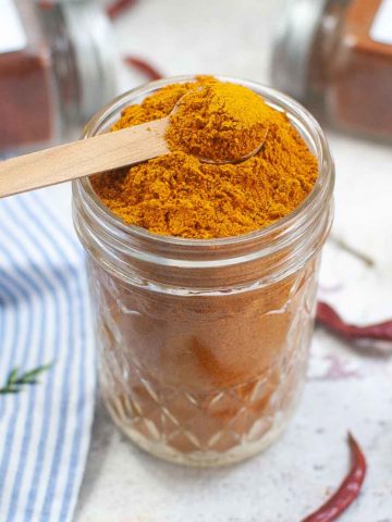 Curry seasoning in mason jar with wooden spoon.