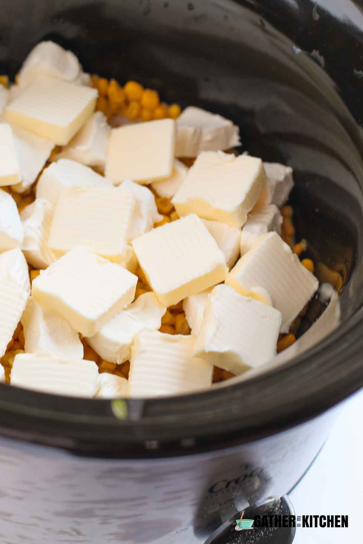 Closeup of butter and cream cheese cubed and on top of the creamed corn in the slow cooker.