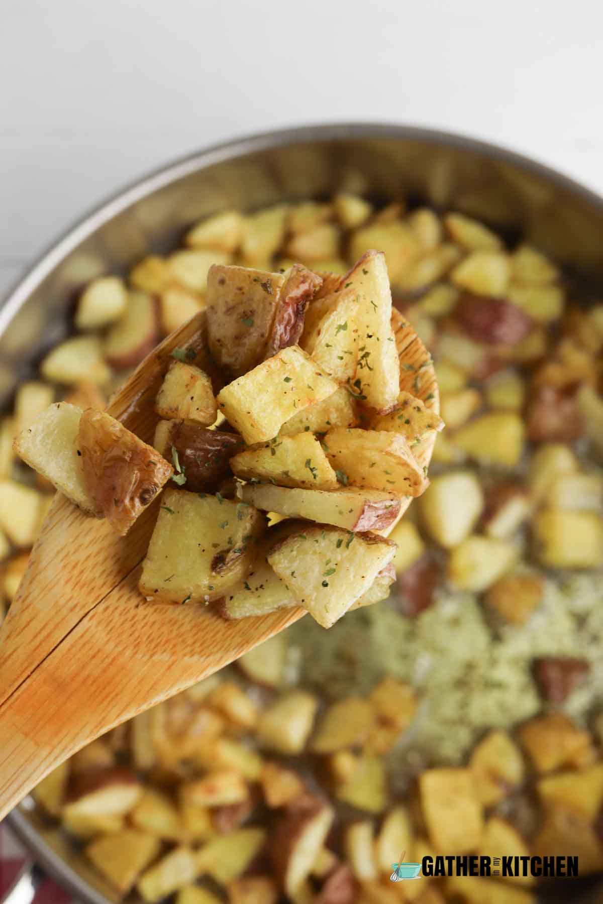 Wooden spoon holding cooked fried potatoes over pan.