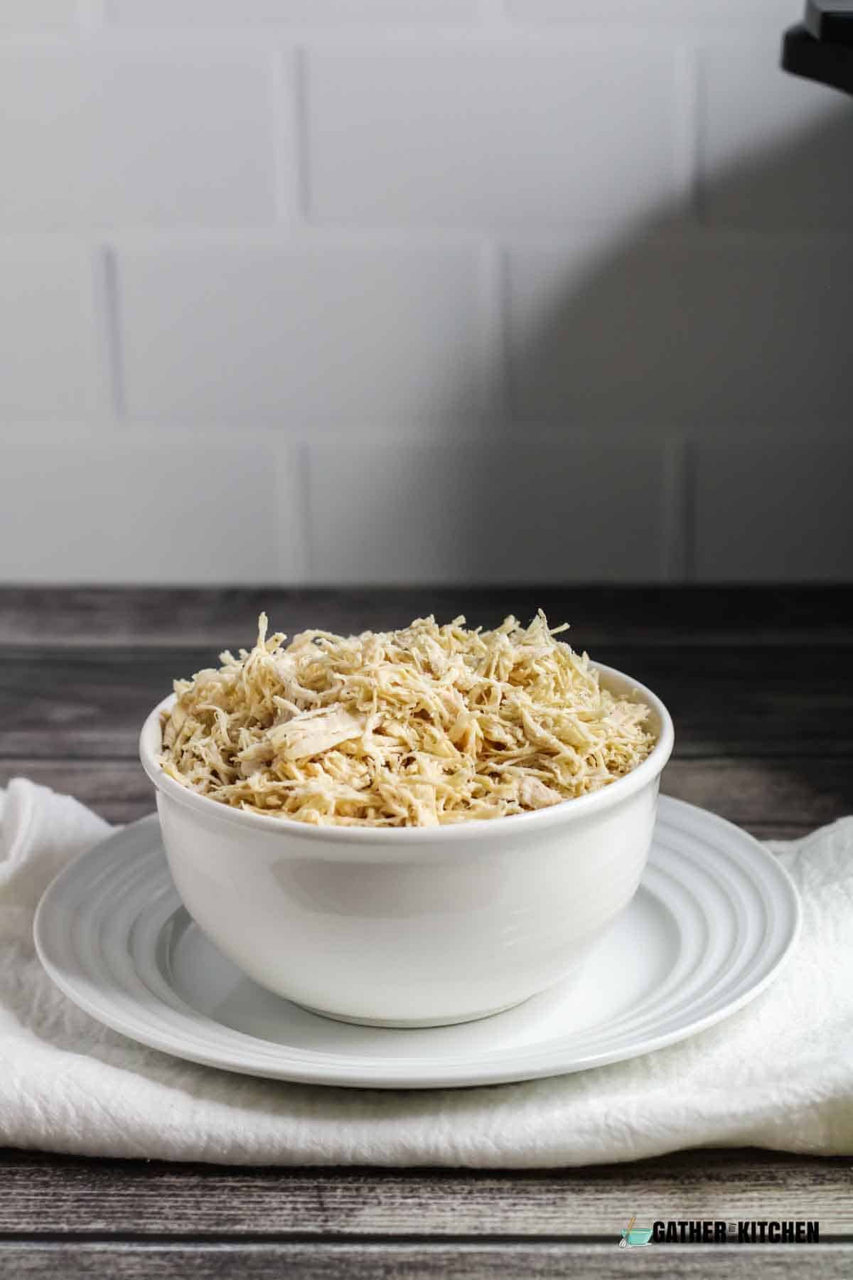 Instant pot shredded chicken in a bowl positioned on a plate.