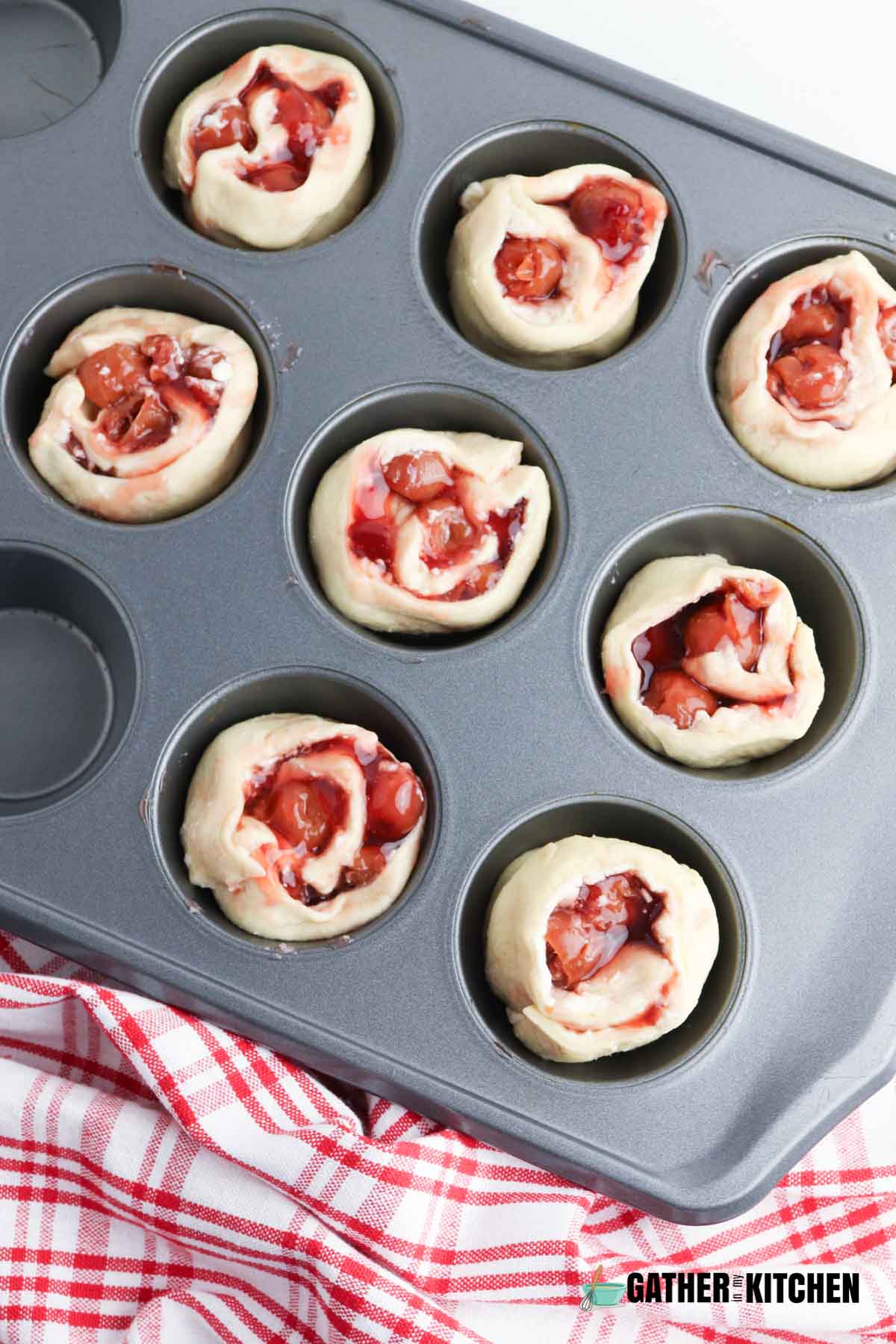 Crescent dough roll slices in cups of muffin tins and you can see the filling inside the rolls of dough.