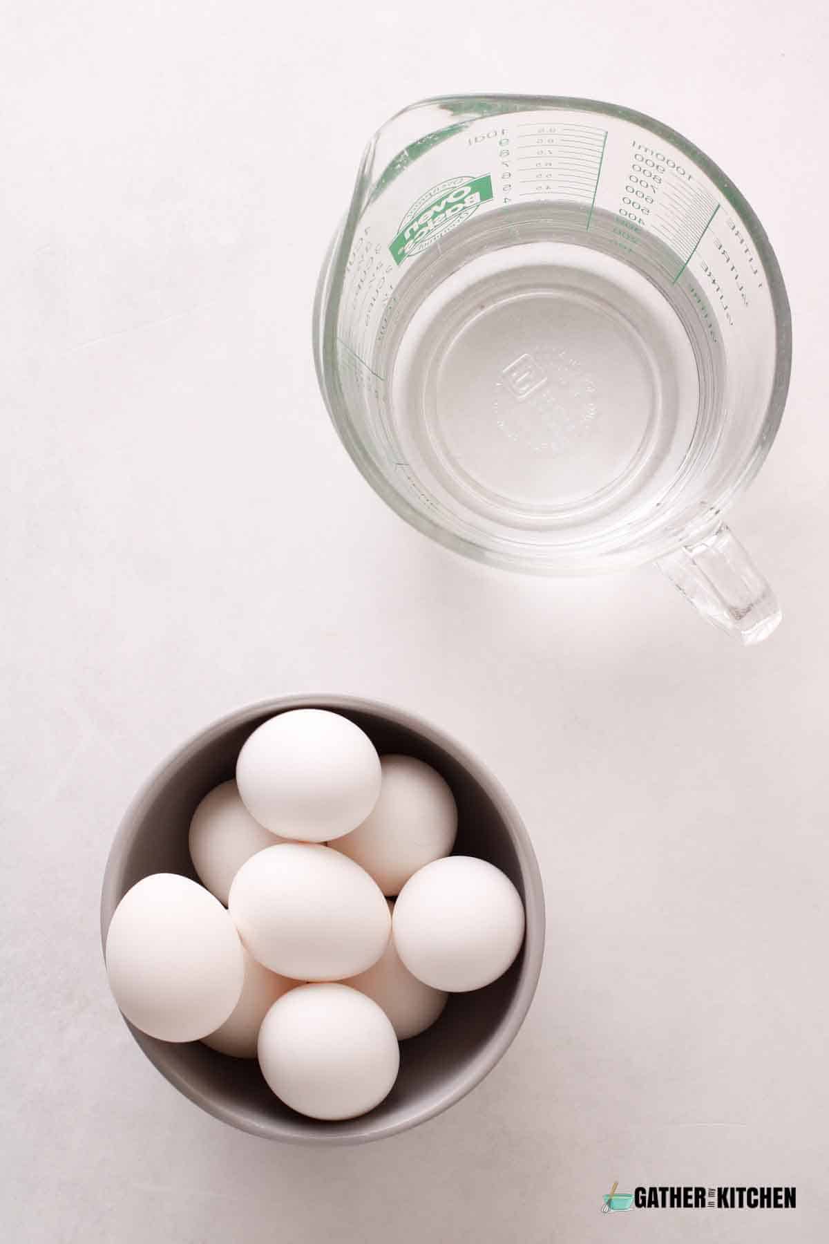 Top down view of eggs in a bowl and a glass measuring cup with water.