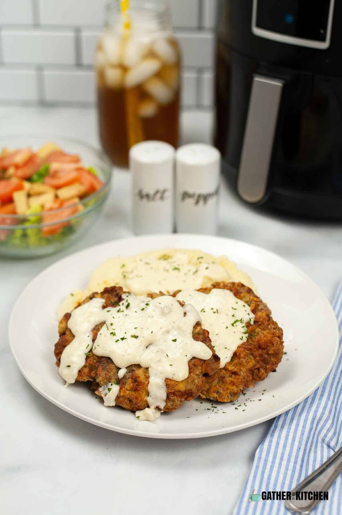Chicken fried steak on a plate with air fryer in the background.