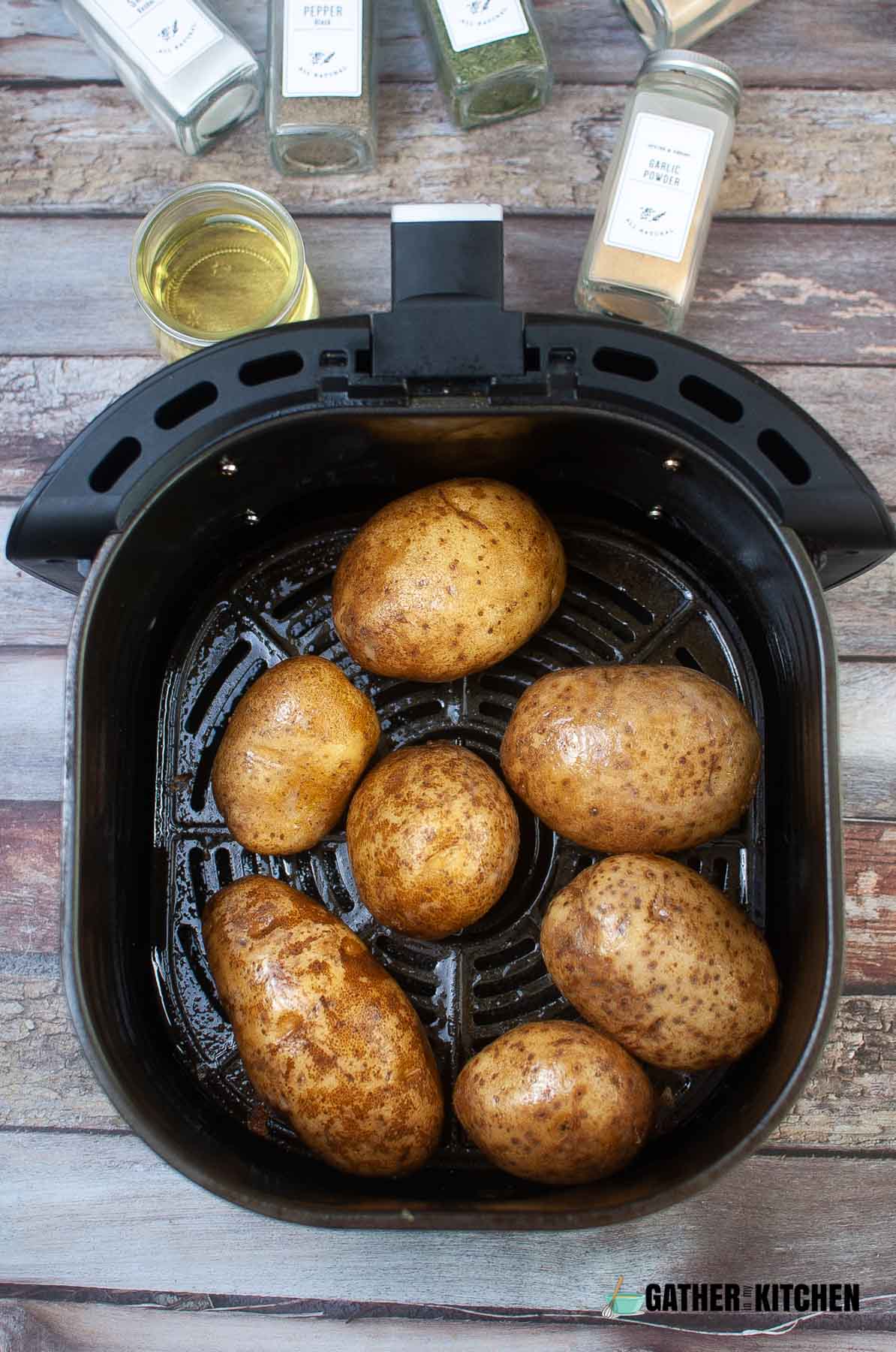 Raw potatoes coated in oil in air fryer basket.