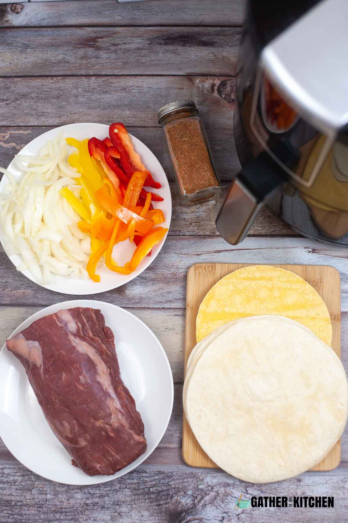 Top down view of plate of sliced onions and bell peppers, container of fajita seasoning, flour and corn tortillas, and beef on a plate.