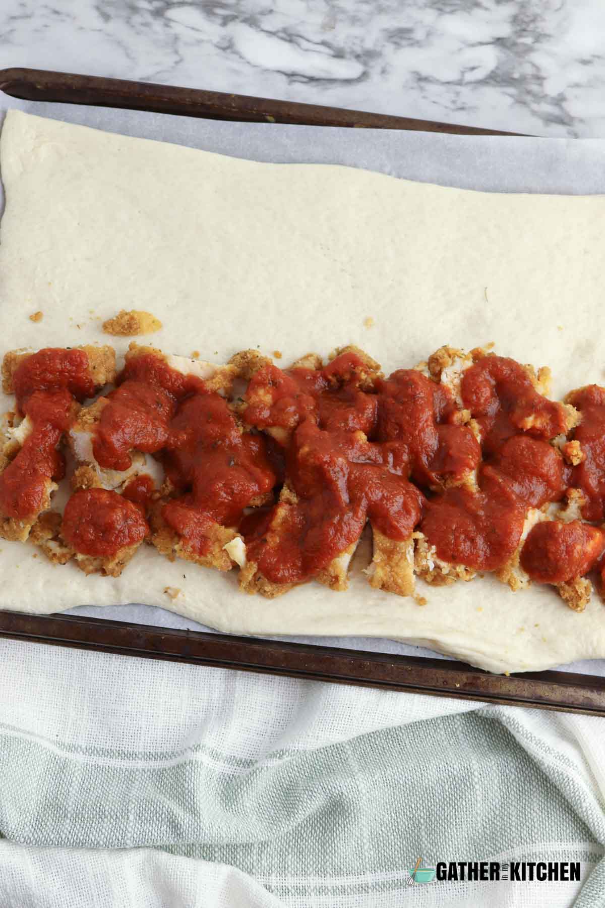 Marinara sauce on top of the cut up chicken on the pizza dough.