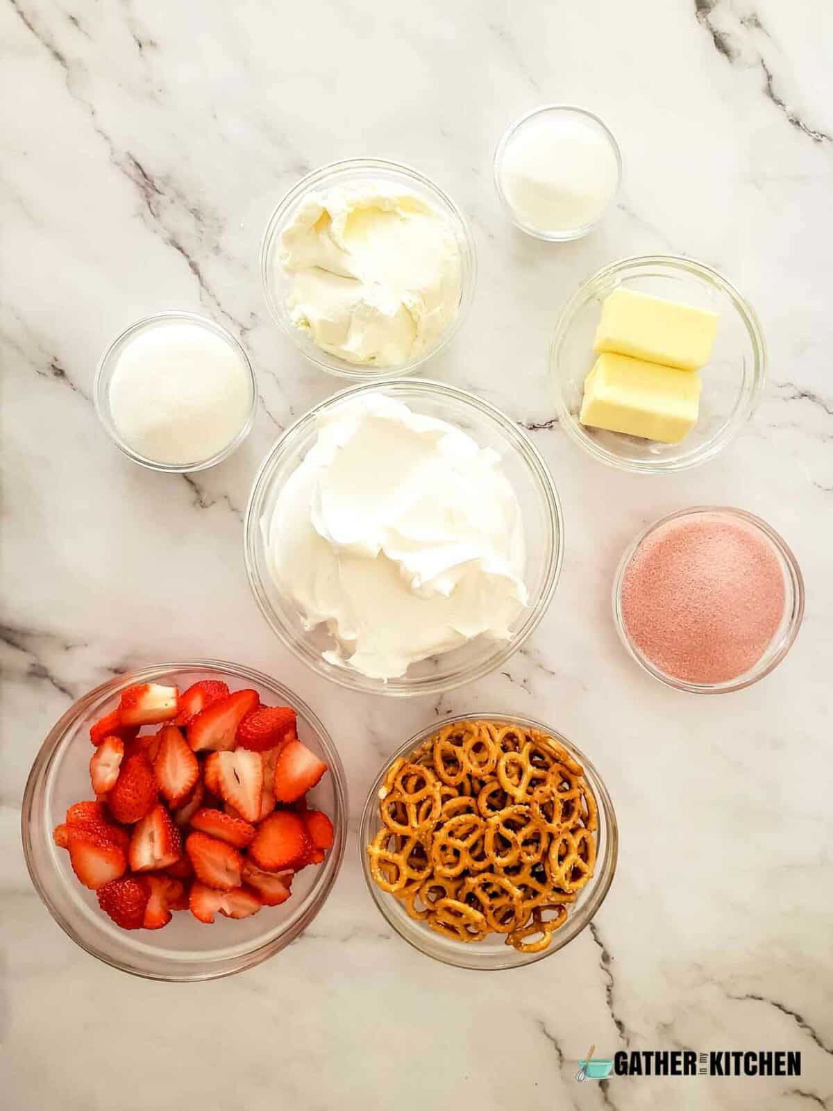 Ingredients for making strawberry pretzel salad: salted pretzels, cut strawberries, sugar, butter, cream cheese, Cool Whip, and contents of a strawberry Jello packet.