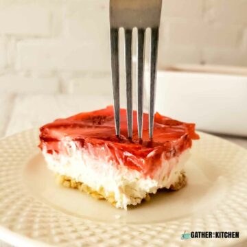 Piece of strawberry pretzel salad on a plate with a fork through it.