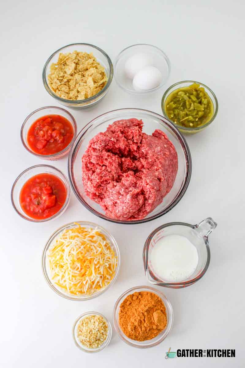 Mexican meatloaf ingredients: tortilla chips, 2 eggs, green chilis, ground chuck, milk, taco seasoning, diced onion, cheese, salsa.
