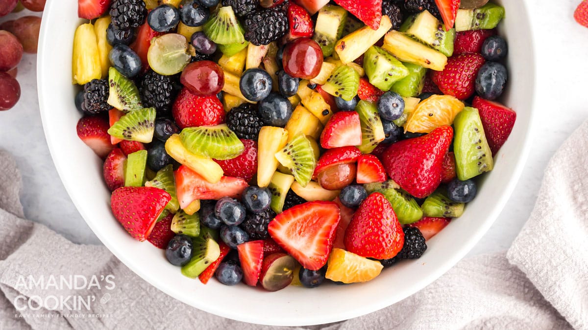 Top down view of a fruit salad with strawberries, kiwi, blueberries, pineapple, oranges, blackberries and grapes.