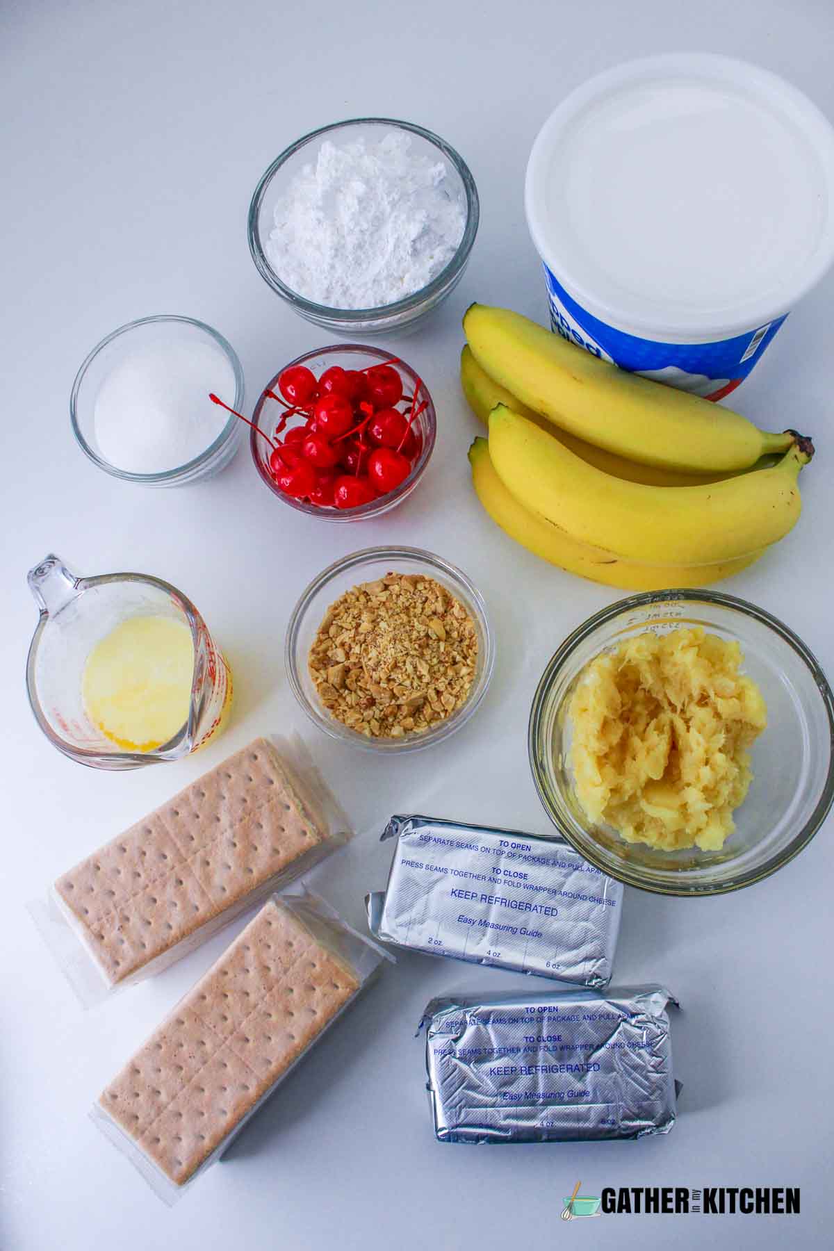 Ingredients for no bake banana split cake: powdered sugar, whipped topping, bananas, crushed pineapples, 2 cream cheese packages, 2 packages of graham crackers, melted butter, peanuts, marasschino cherries, sugar.