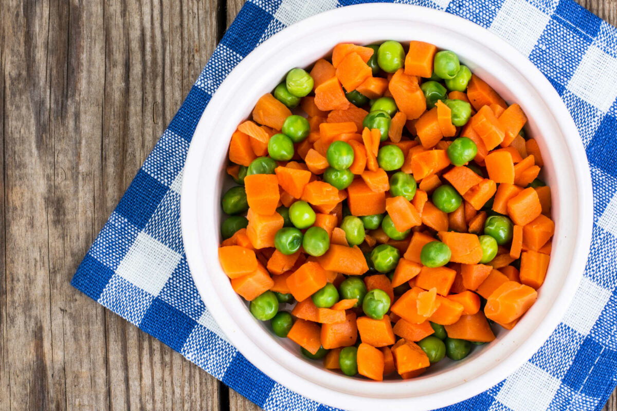 Steamed carrots and peas in a white bowl.