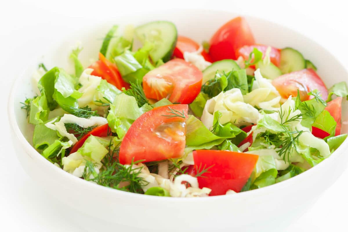 Closeup of a side salad in a bowl with lettuce, tomatoes and cucumbers.