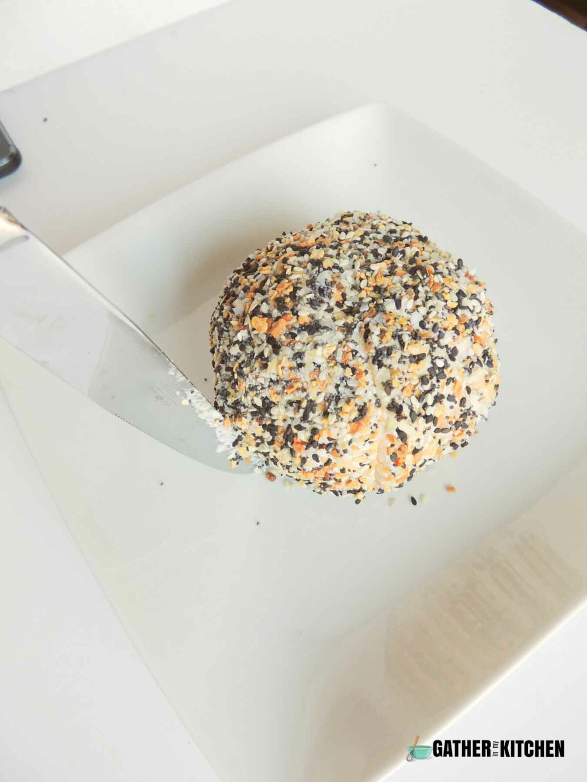 A butter knife being used to score the sides of the pumpkin cheese ball.