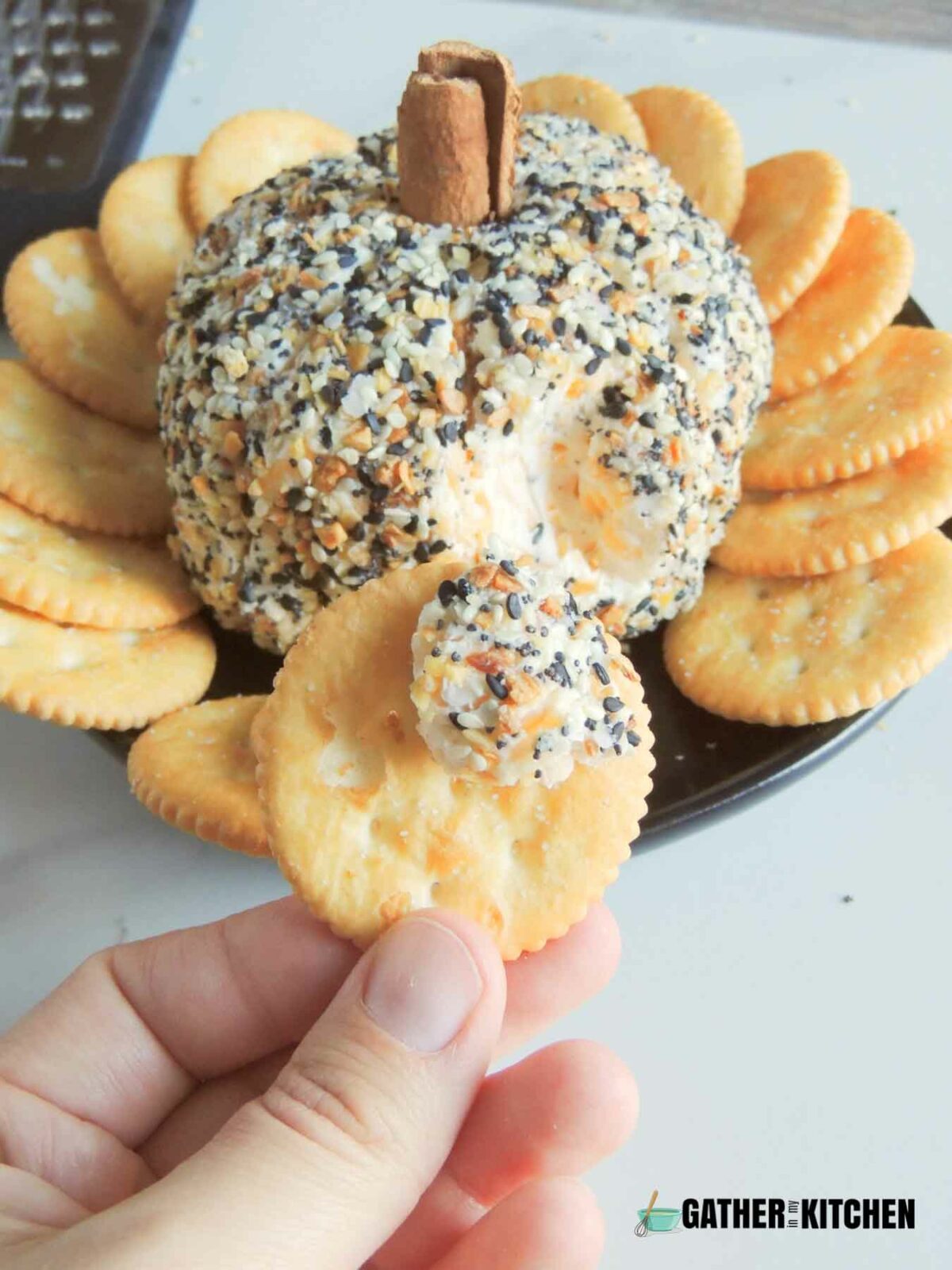Ritz cracker in front of pumpkin cheese ball with cheese dip on it.