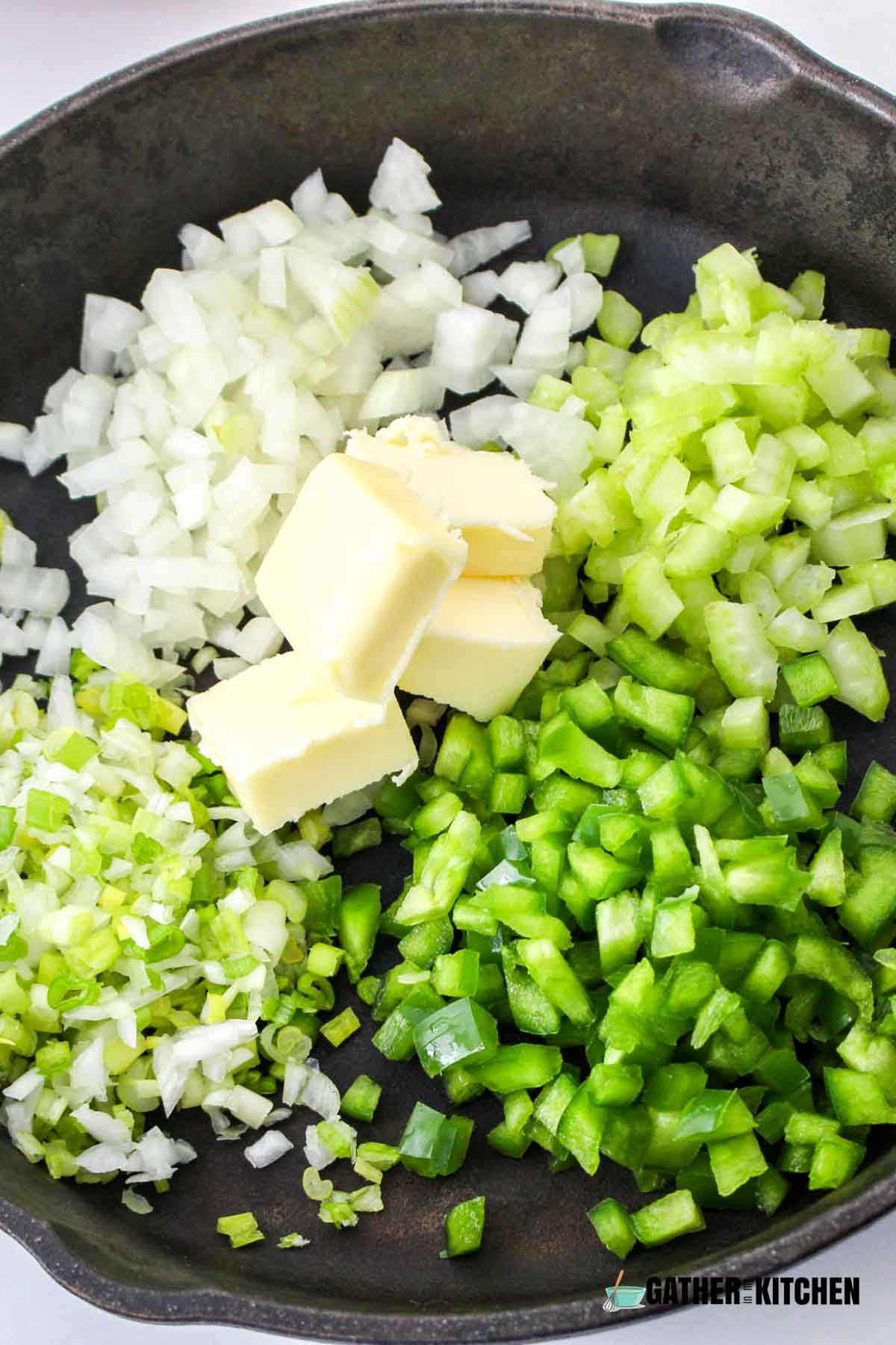 A skillet with green onions, onions, celery, bell pepper and butter.