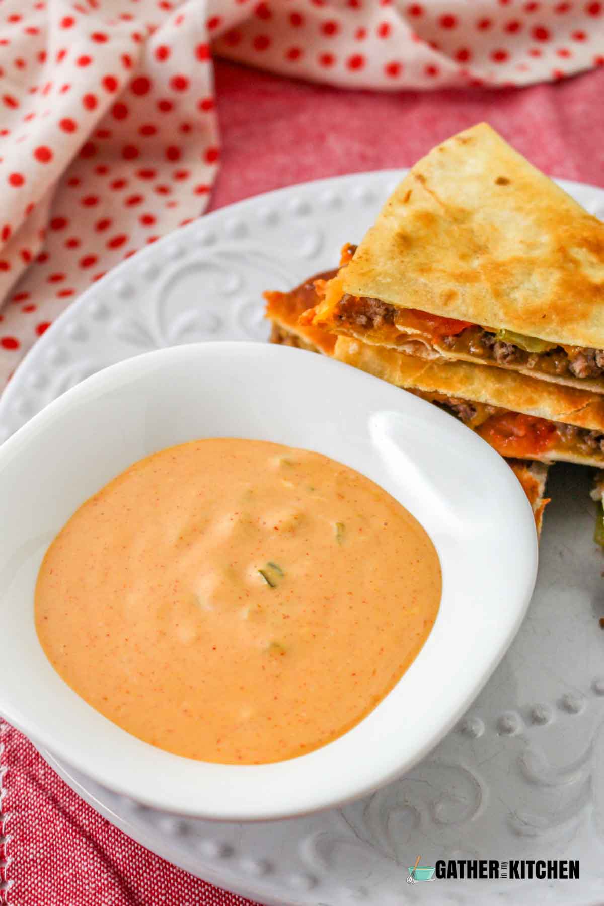 A small bowl of dip on a plate with quesadillas.