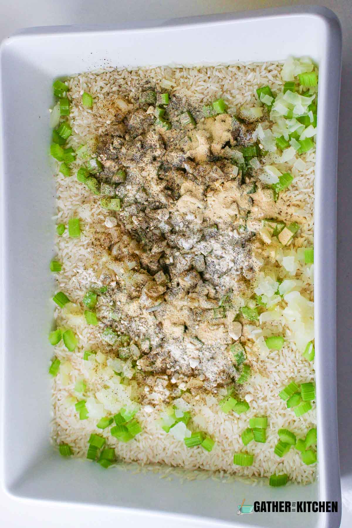 A tray filled with rice with diced celery, onion and seasonings on top.