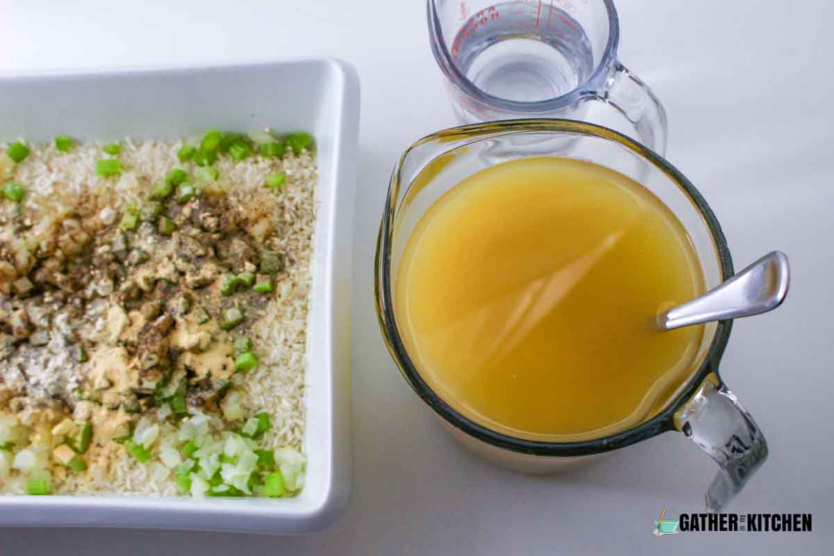 A tray of rice beside a cup of water and chicken broth.
