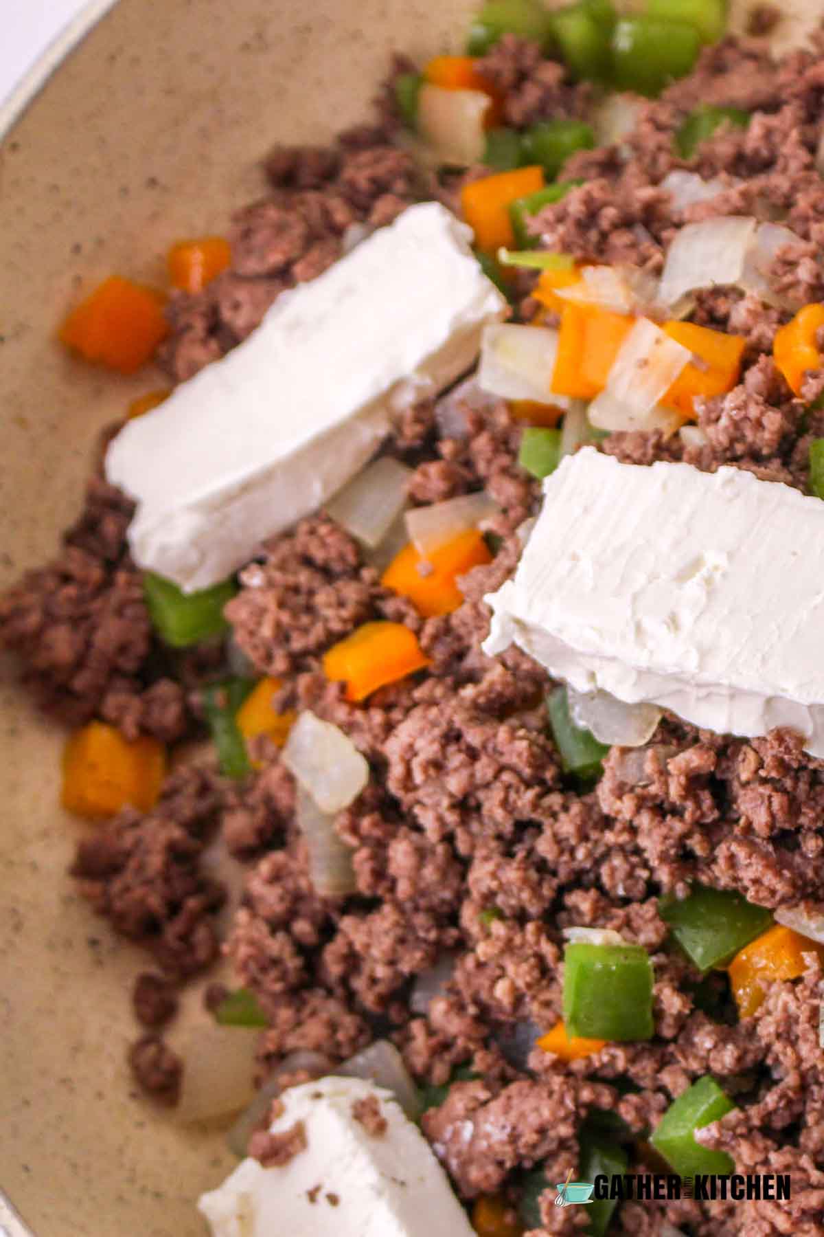Slices of cream cheese on top of ground beef, onions and bell peppers.