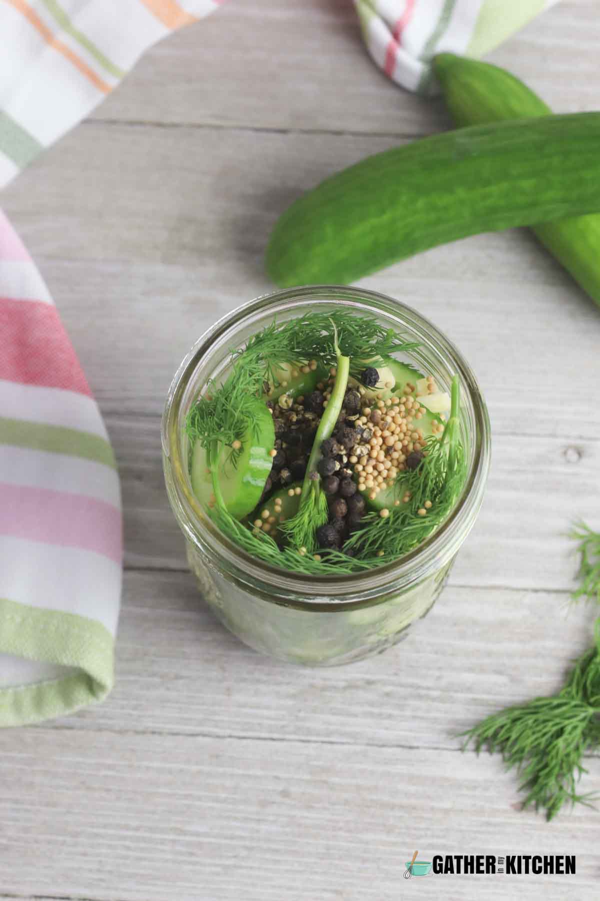 A jar filled with cucumbers, garlic, herbs, and seasonings.