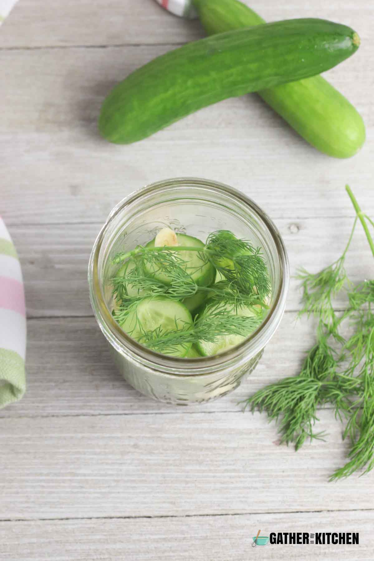 A jar filled with cucumbers, garlic, and herbs.