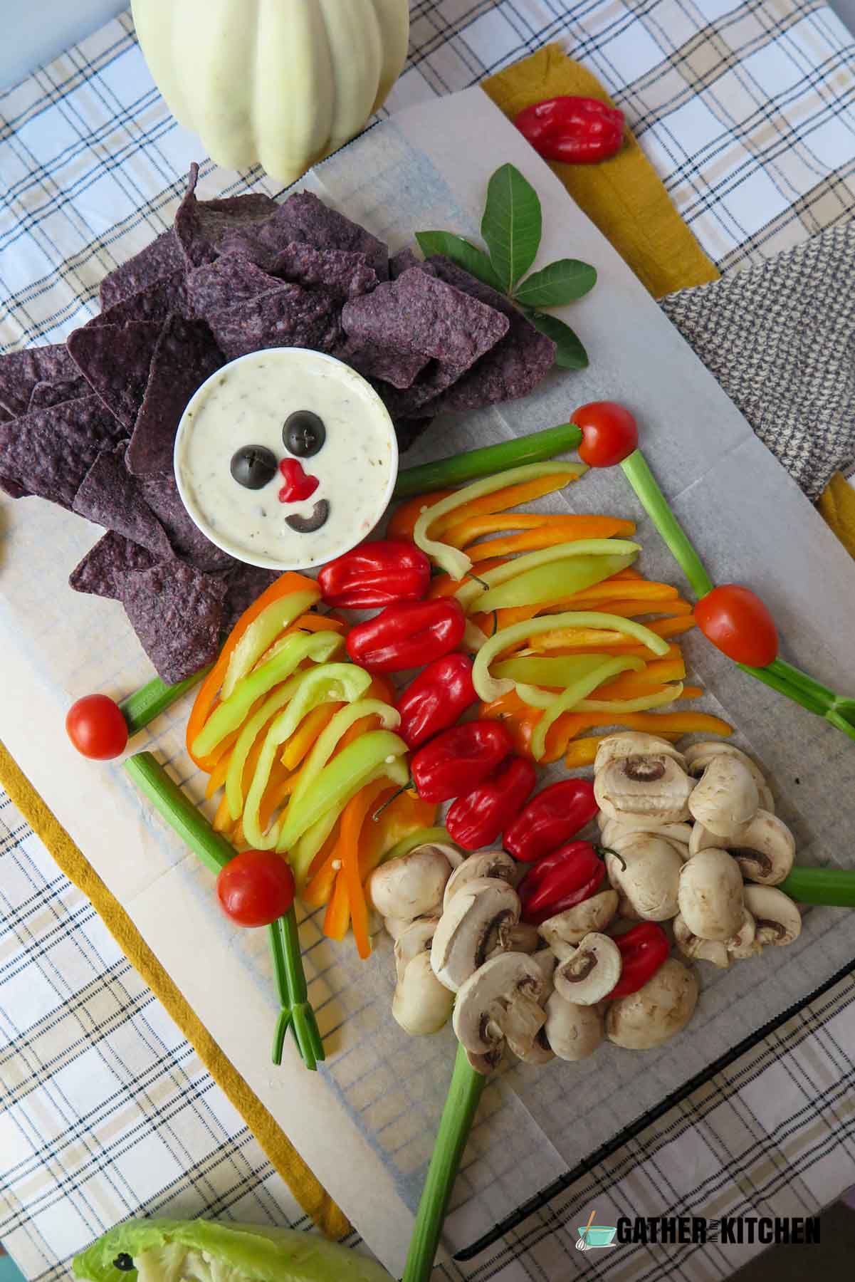 A tray with chips, veggies and a bowl of dip forming a skeleton.