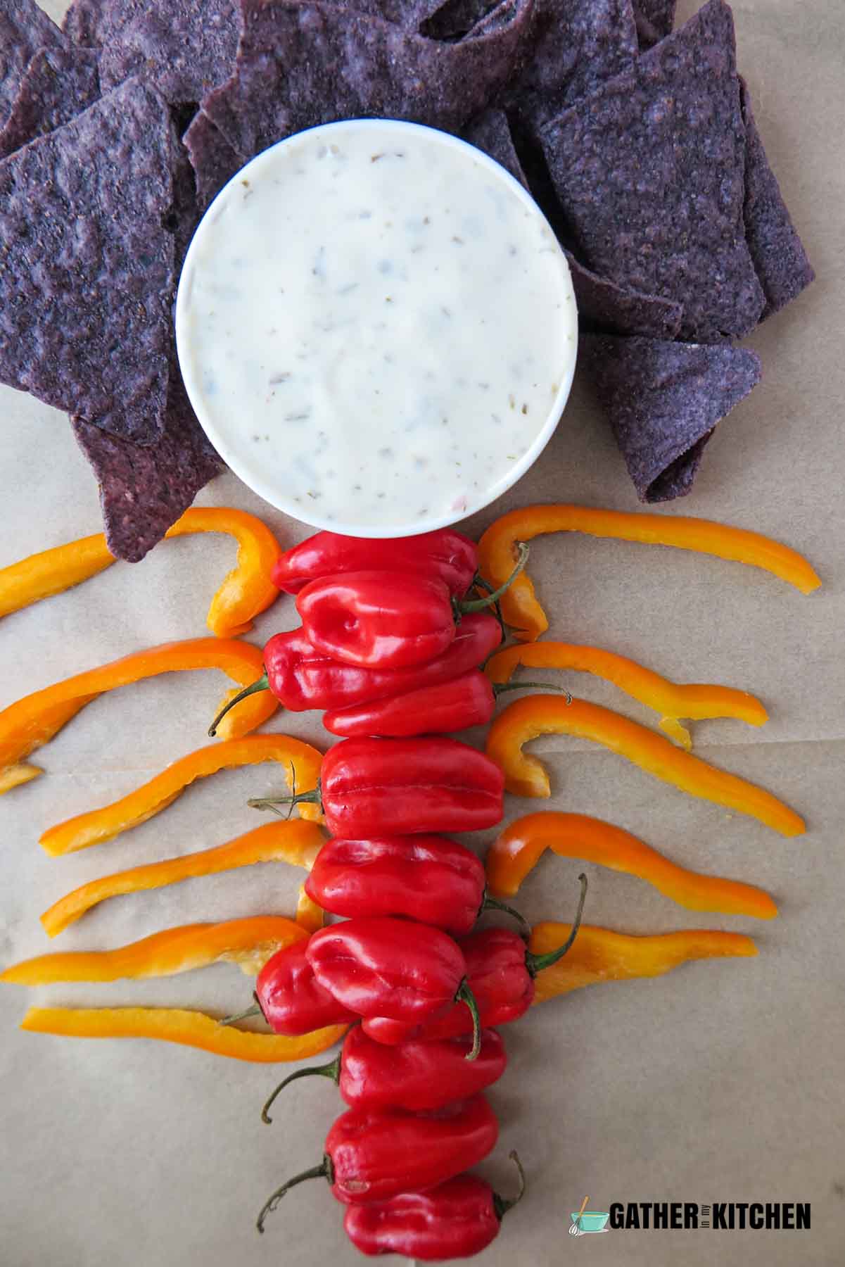 A bowl of dip with chips surrounding it and bell peppers arranged like a spine and rib cage.
