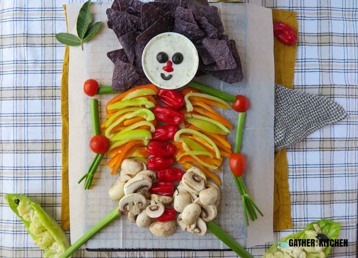Chips, veggies, dip, and mushrooms arranged to form a skeleton on parchment paper.