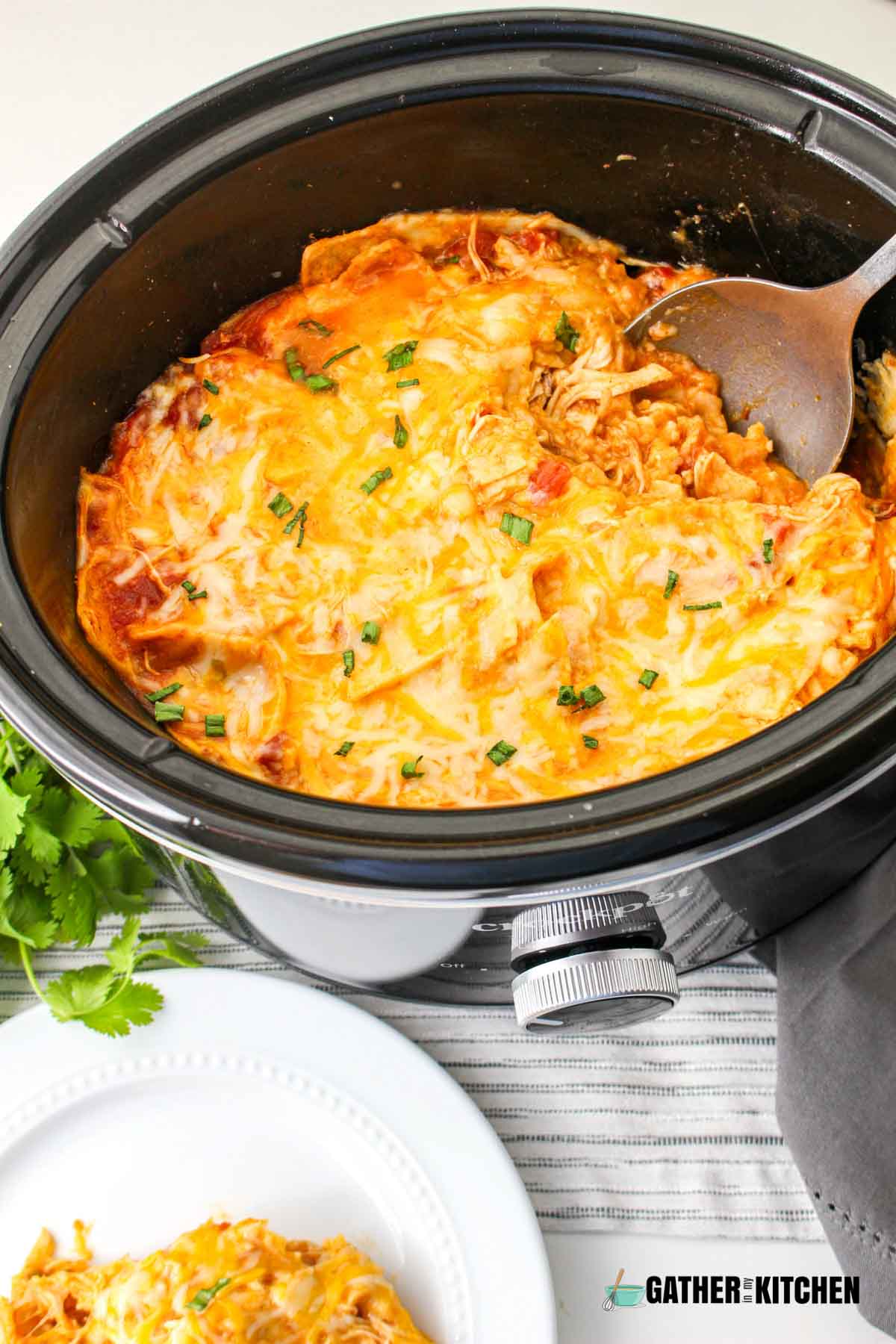 Enchilada casserole in a slow cooker with a spoon in it.