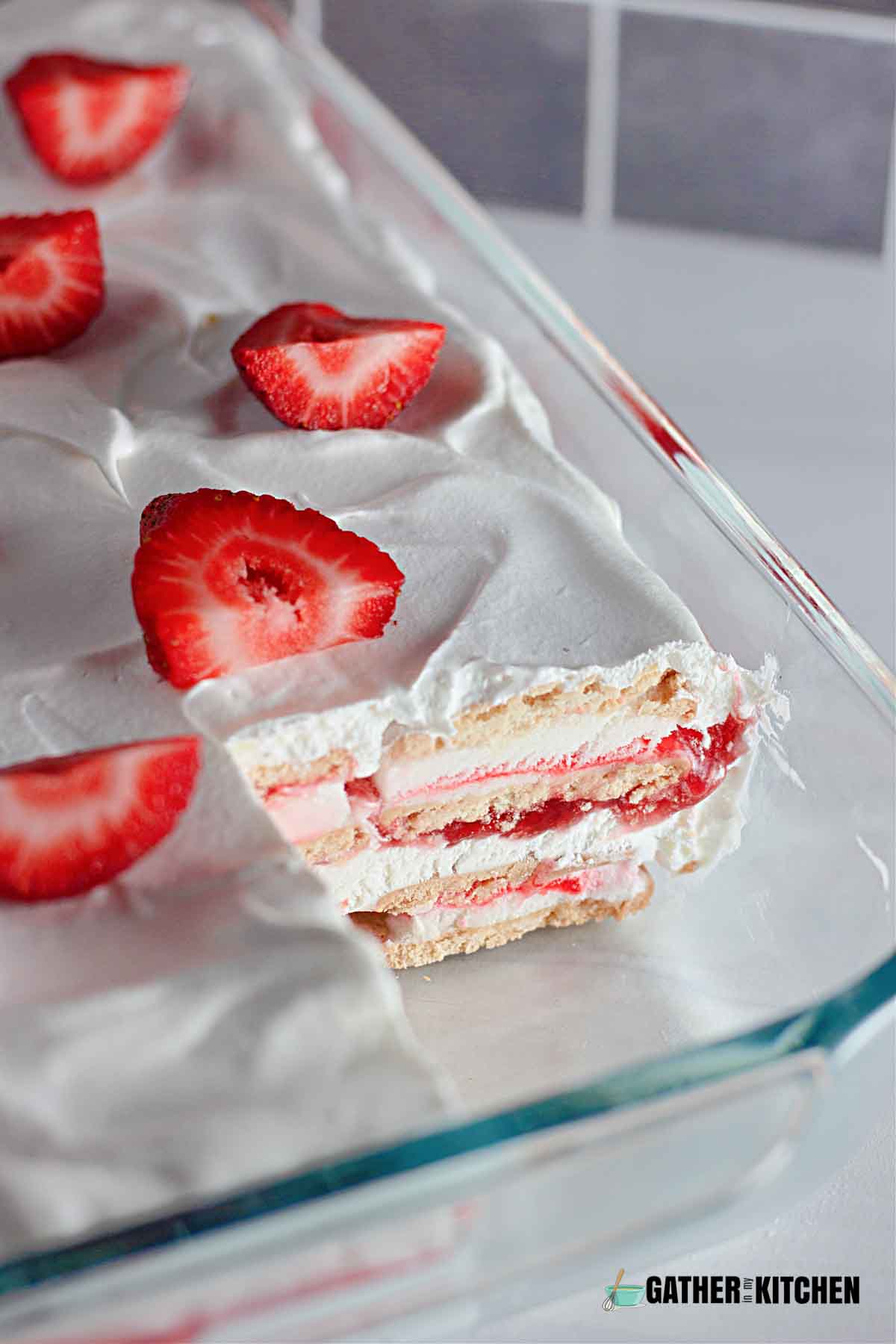 A closeup of a casserole dish of strawberry ice cream cake with a square slice taken out.